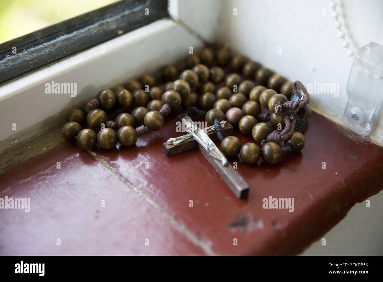 A crucifix and rosary beads lie on a windowsill in St Cuthbert's Hermitage in Lincolnshire, north east Britain April 27, 2015. Denton, a Catholic hermit, rises early to tend to her vegetable garden, feed her cats and pray. But the former Carmelite nun, who in 2006 pledged to live the rest of her life in solitude, has another chore - to update her Twitter account and check Facebook. 'The myth you often face as a hermit is that you should have a beard and live in a cave. None of which is me,' says the ex-teacher. For the modern-day hermit, she says social media is vital: 'tweets are rare, but pr Stock Photo