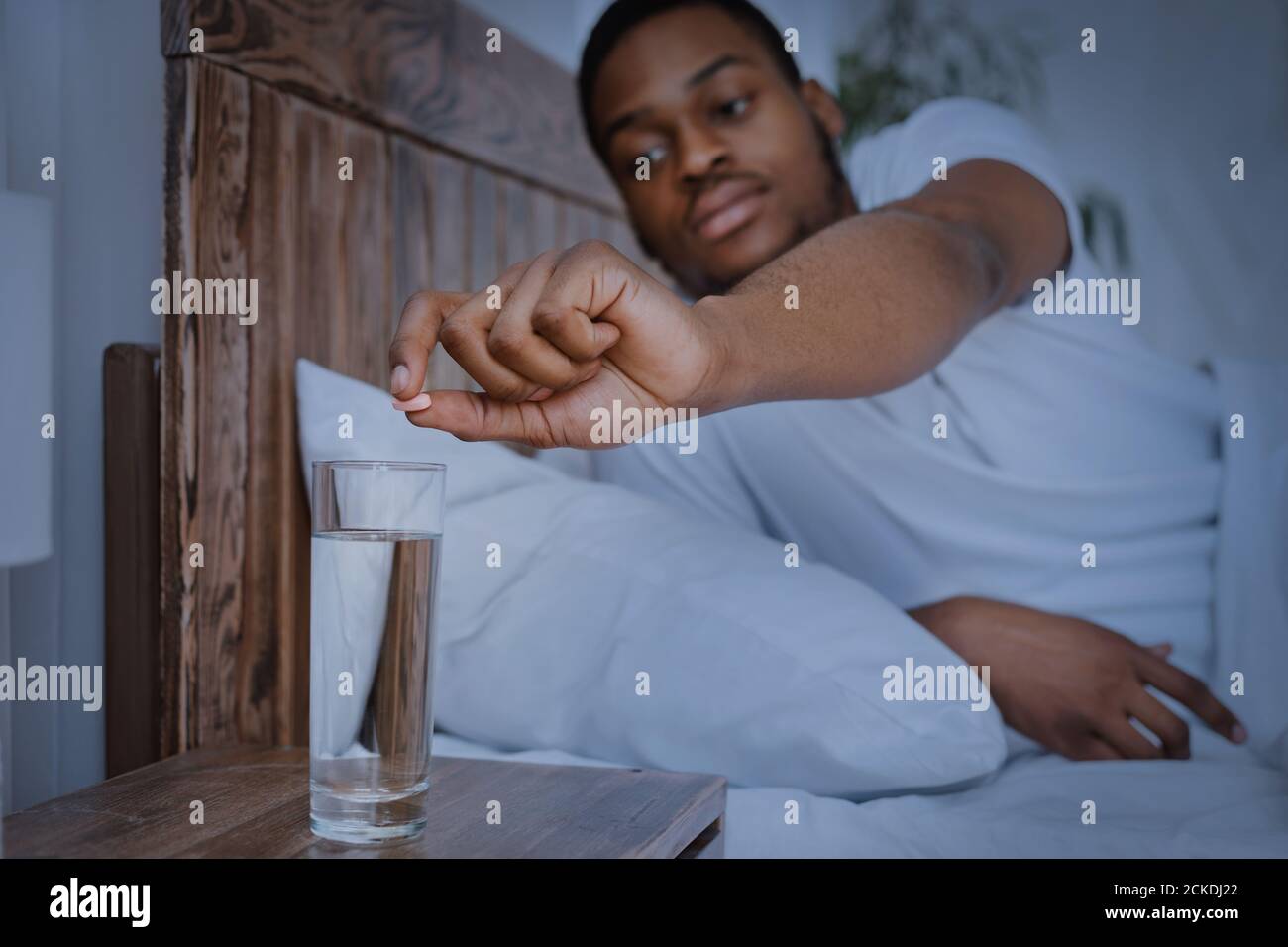 Black Man Taking Medicine Pill Lying In Bed At Home Stock Photo