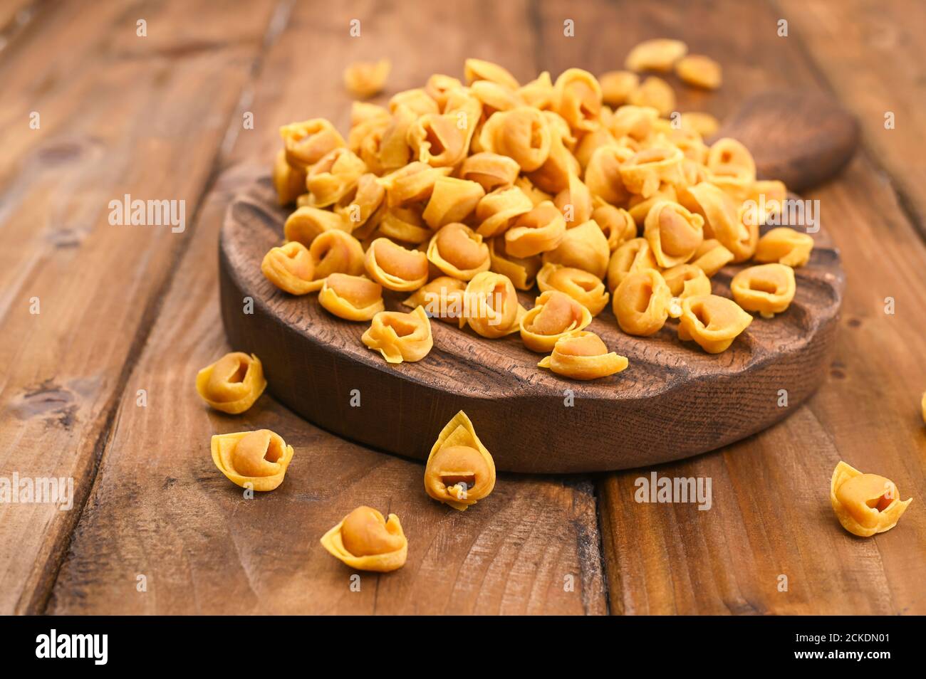Tortellini mignon on a wooden board and parmesan. Specialties of the cuisine from Bologna and Emilia Romagna: Cappelletti, fresh egg pasta with meat and vegetables filling. Copy space Stock Photo
