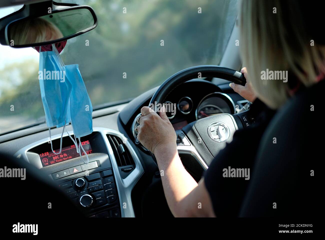 female driver driving car with face masks hanging from rear view mirror, norfolk, england Stock Photo