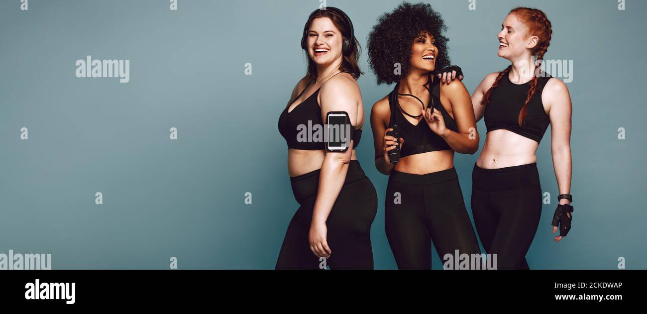 Multi-ethnic group of women together against grey background and smiling. Diverse group females in sportswear after workout. Stock Photo