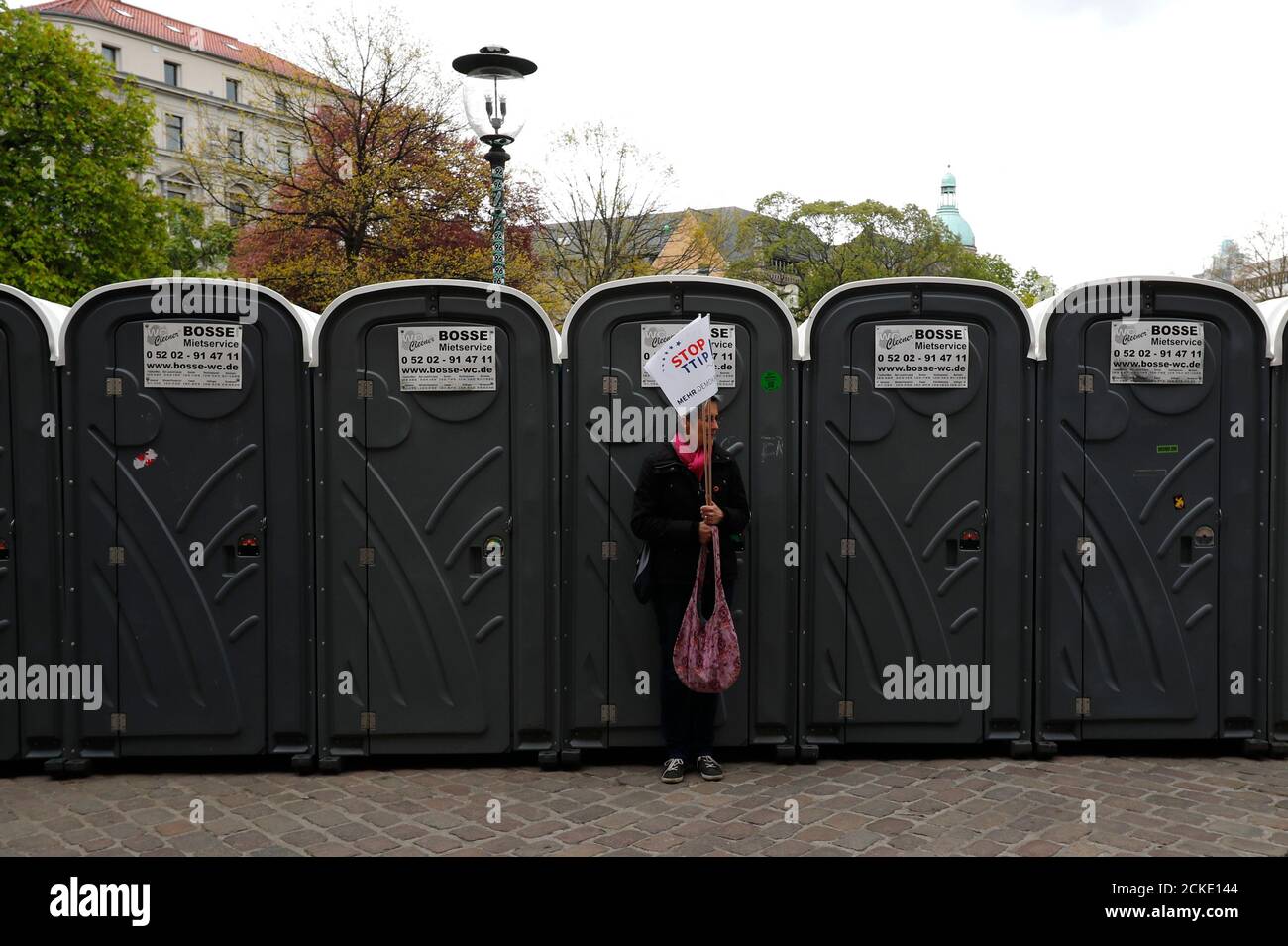 A protester holds placard as she stands in front of mobile toilets during a demonstration against Transatlantic Trade and Investment Partnership (TTIP) free trade agreement ahead of U.S. President Barack Obama's visit in Hannover, Germany April 23, 2016.  REUTERS/Kai Pfaffenbach Stock Photo