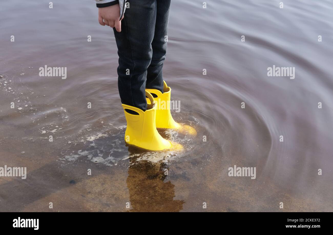 girl wearing yellow rain boots standing in a puddle. cropped view ...
