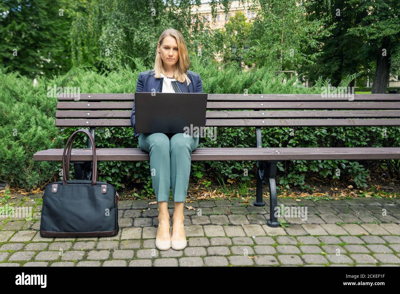 young businesswoman sitting on the bench in the city park and working on laptop. outdoor office freelance work Stock Photo