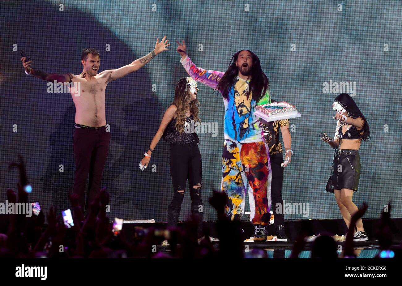 DJ Steve Aoki (C) throws cake into people's faces during the iHeartRadio Music Festival at T