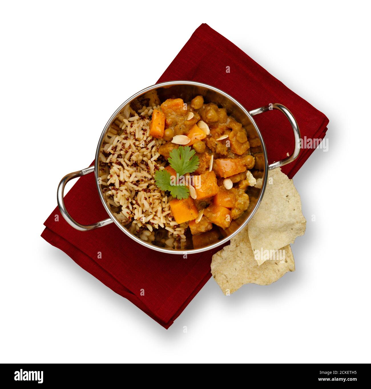 A traditional blati dish filled with delicious vegetable chicken curry and rustic rice, garnished with a sprig of corriander, on a red napkin and popa Stock Photo
