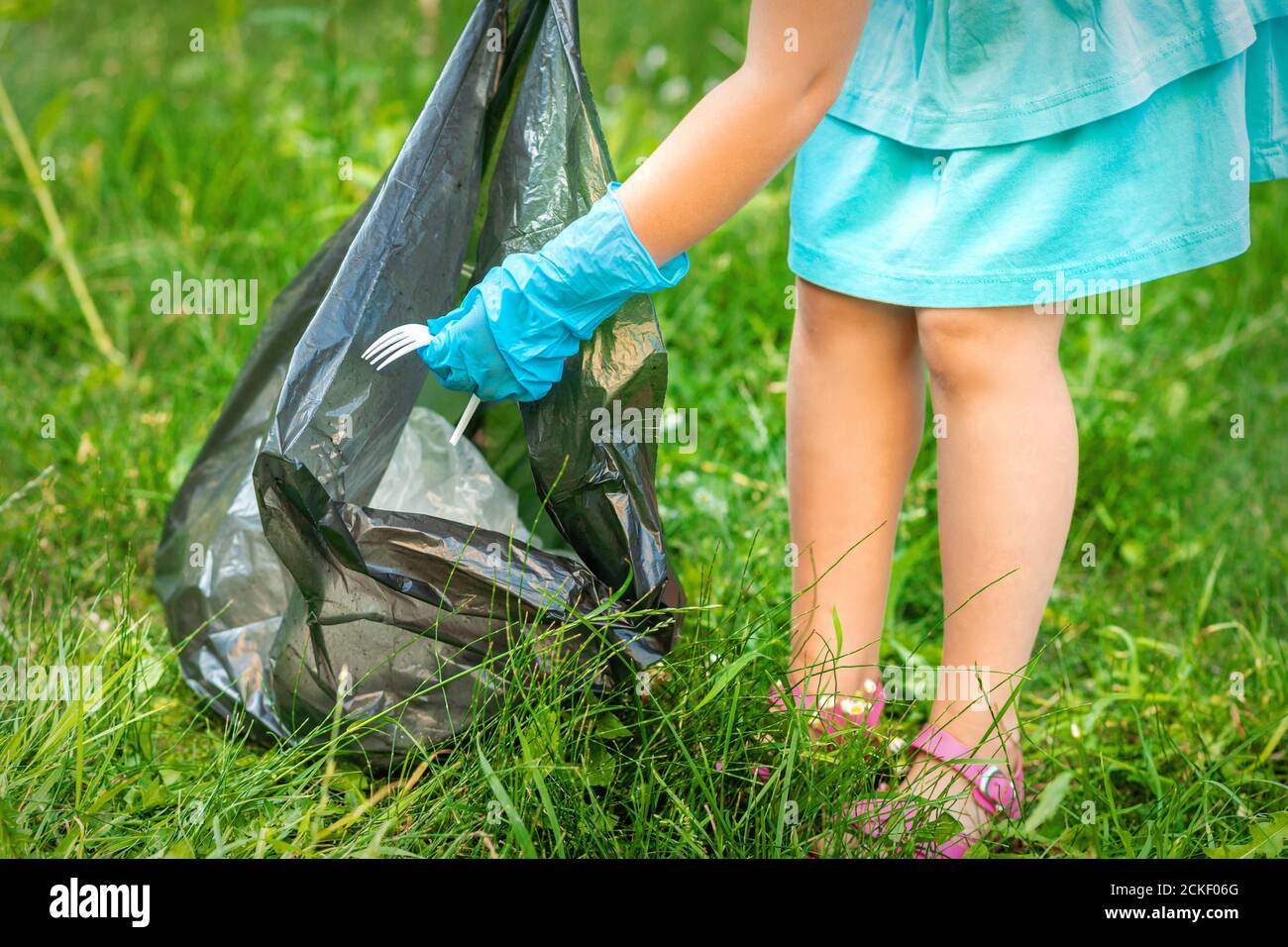 Child collects plastic trash from grass throwing garbage in garbage bag
