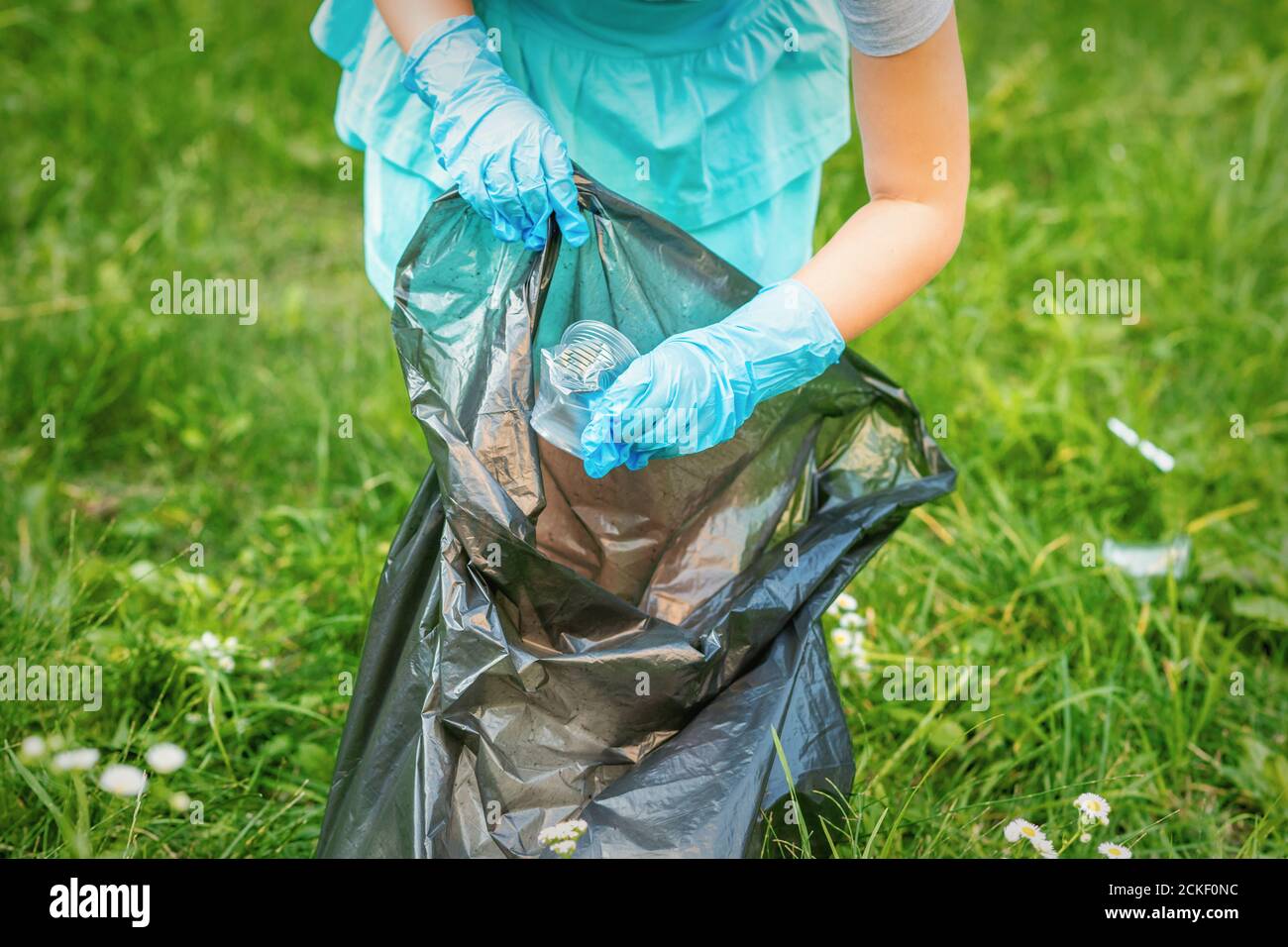 Child collects plastic trash from grass throwing garbage in garbage bag