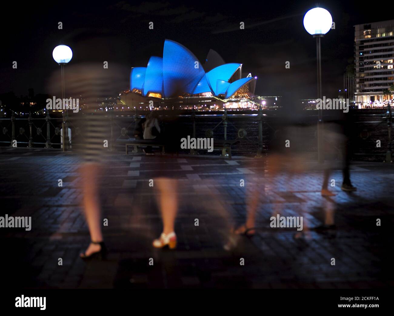A group of women visiting Sydney's waterfront walk past the Sydney Opera House illuminated in a shade of blue October 24, 2015. Around 200 iconic monuments, buildings, museums, bridges and other landmarks in nearly 60 countries including Australia's architectural icon, will be lit up blue, the official colour of the United Nations, as part of a global campaign to commemorate its 70th anniversary.  REUTERS/Jason Reed Stock Photo
