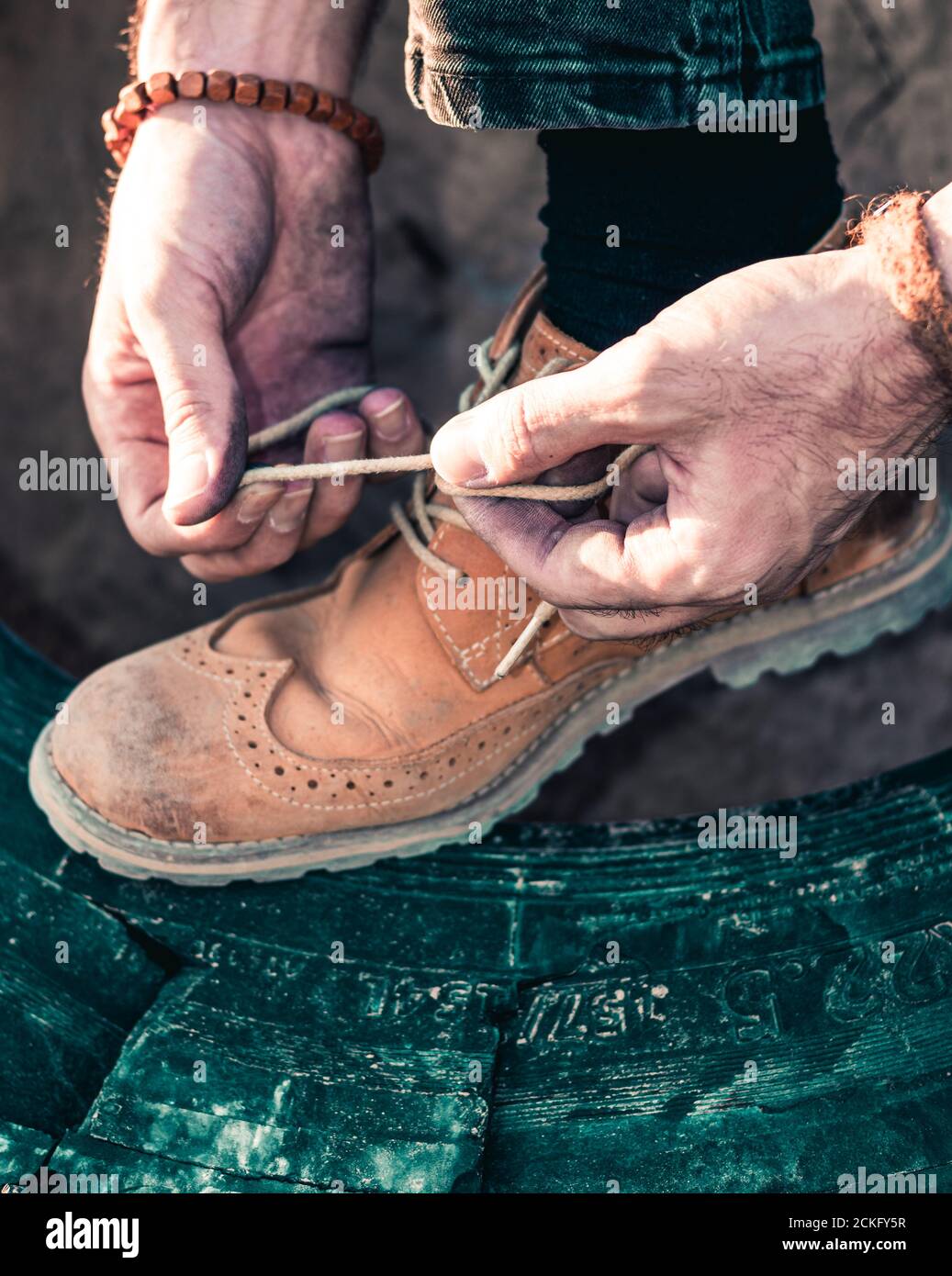 a man ties shoelaces on top of a truck tire Stock Photo