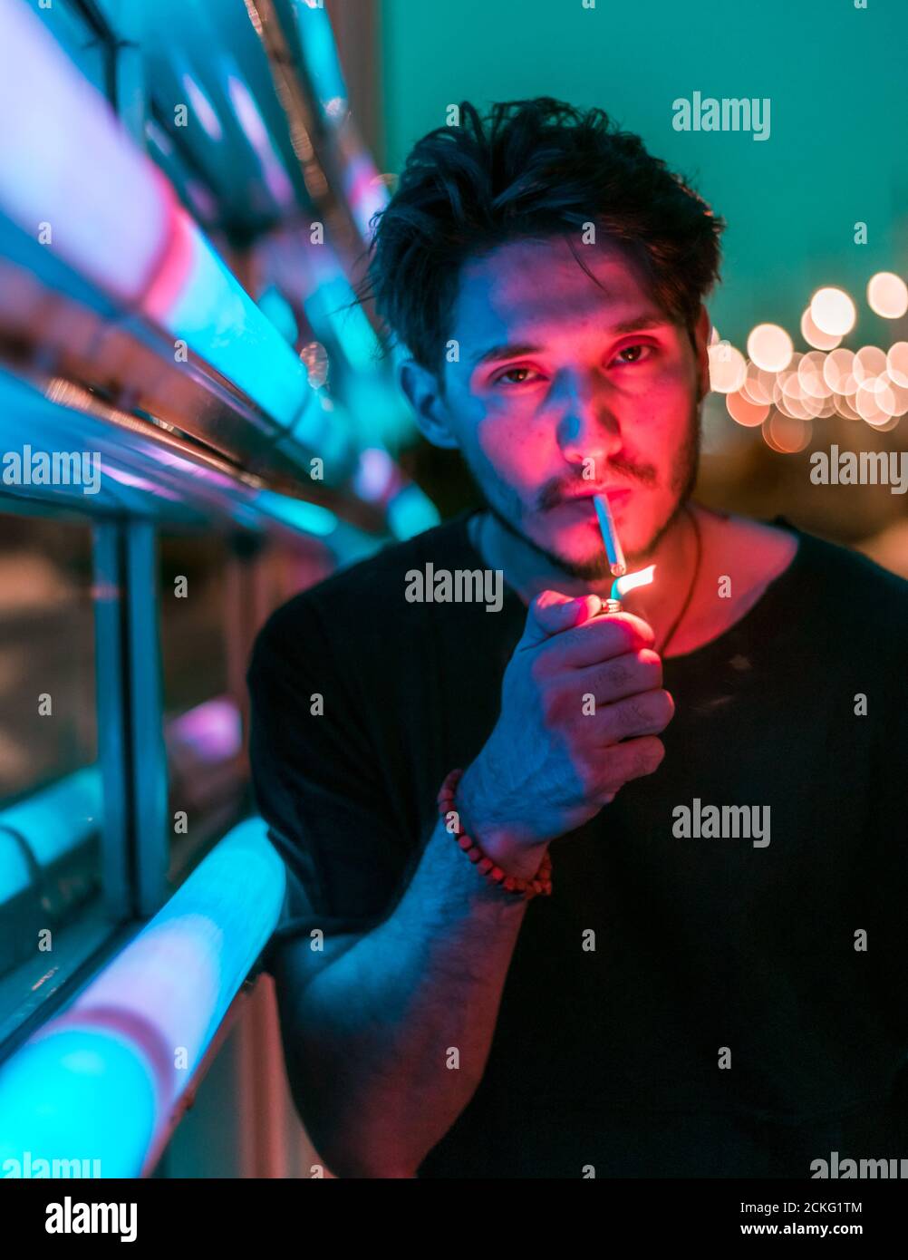 a young handsome man leaning on the neon display at night and lighting a cigarette Stock Photo