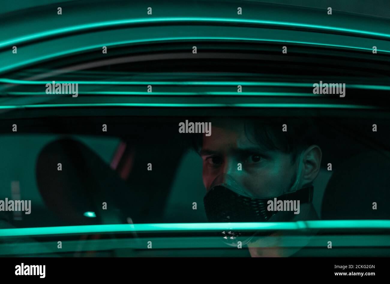 a young man in a face mask driving a car in the night city with neon lights reflecting from the glass of his car Stock Photo