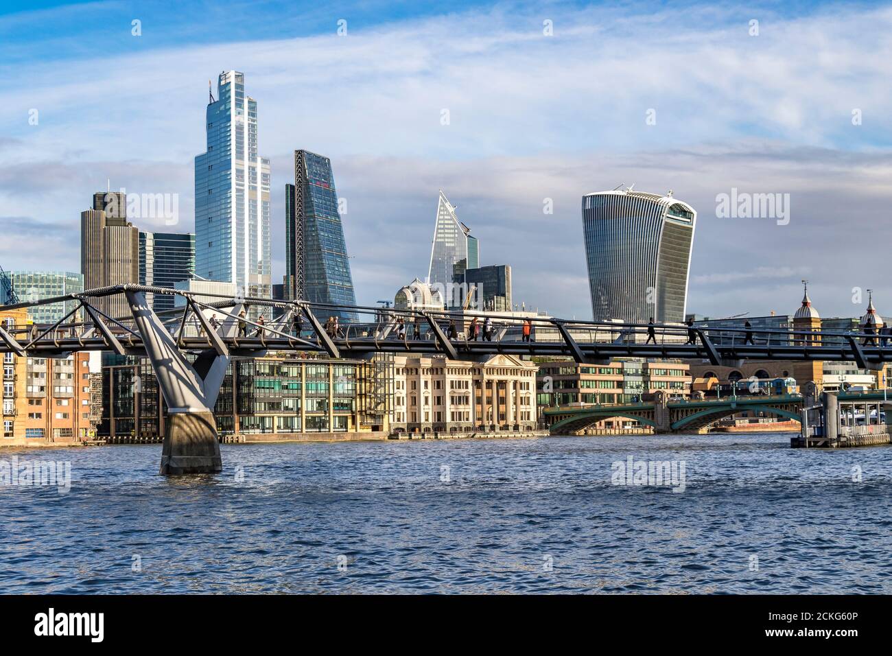 People crossing The Millennium Bridge, a footbridge across The River Thames with The City Of London skyline in the background , London,UK Stock Photo