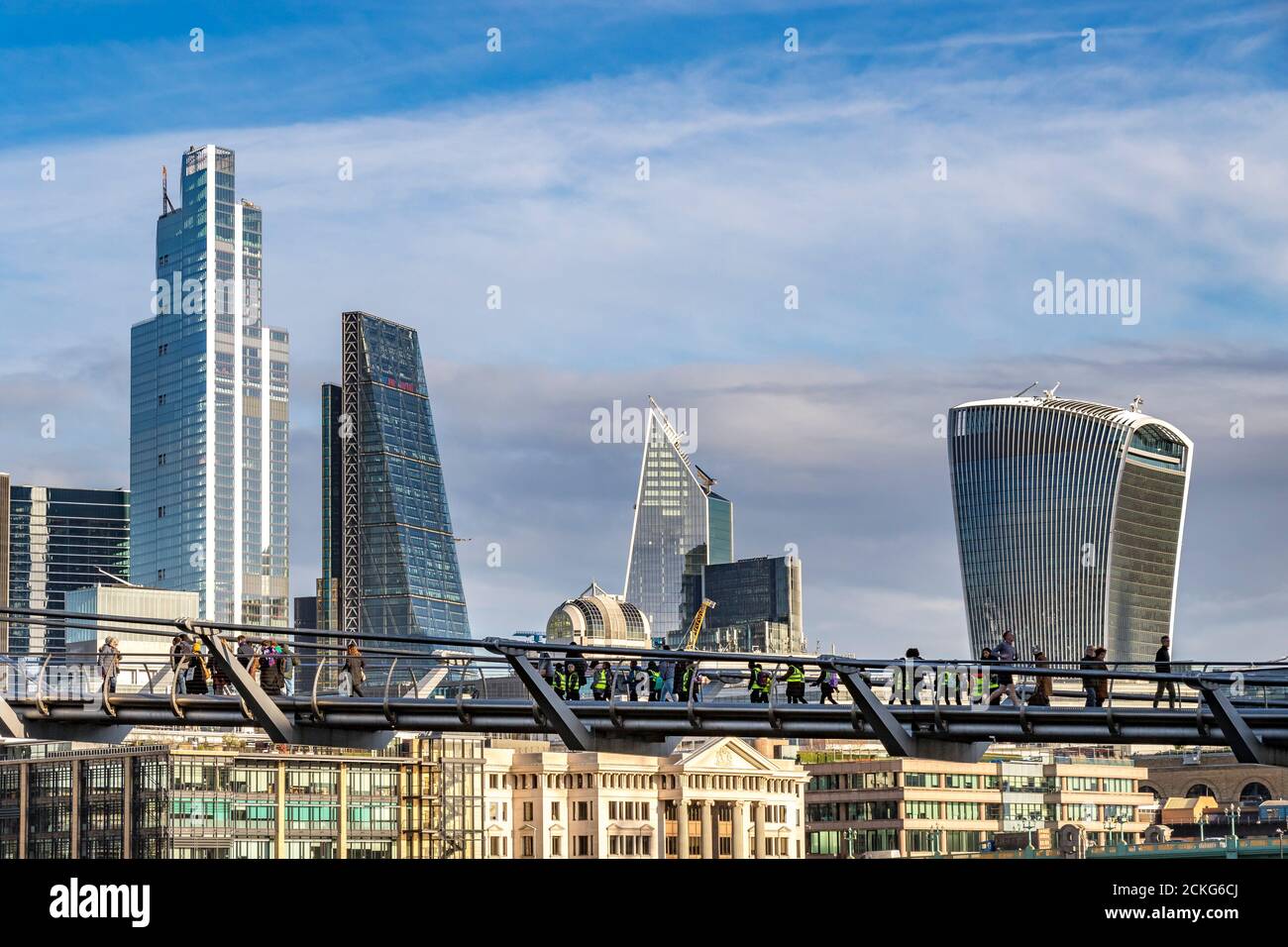 People crossing The Millennium Bridge, a footbridge across The River Thames with The City Of London skyline in the background , London,UK Stock Photo