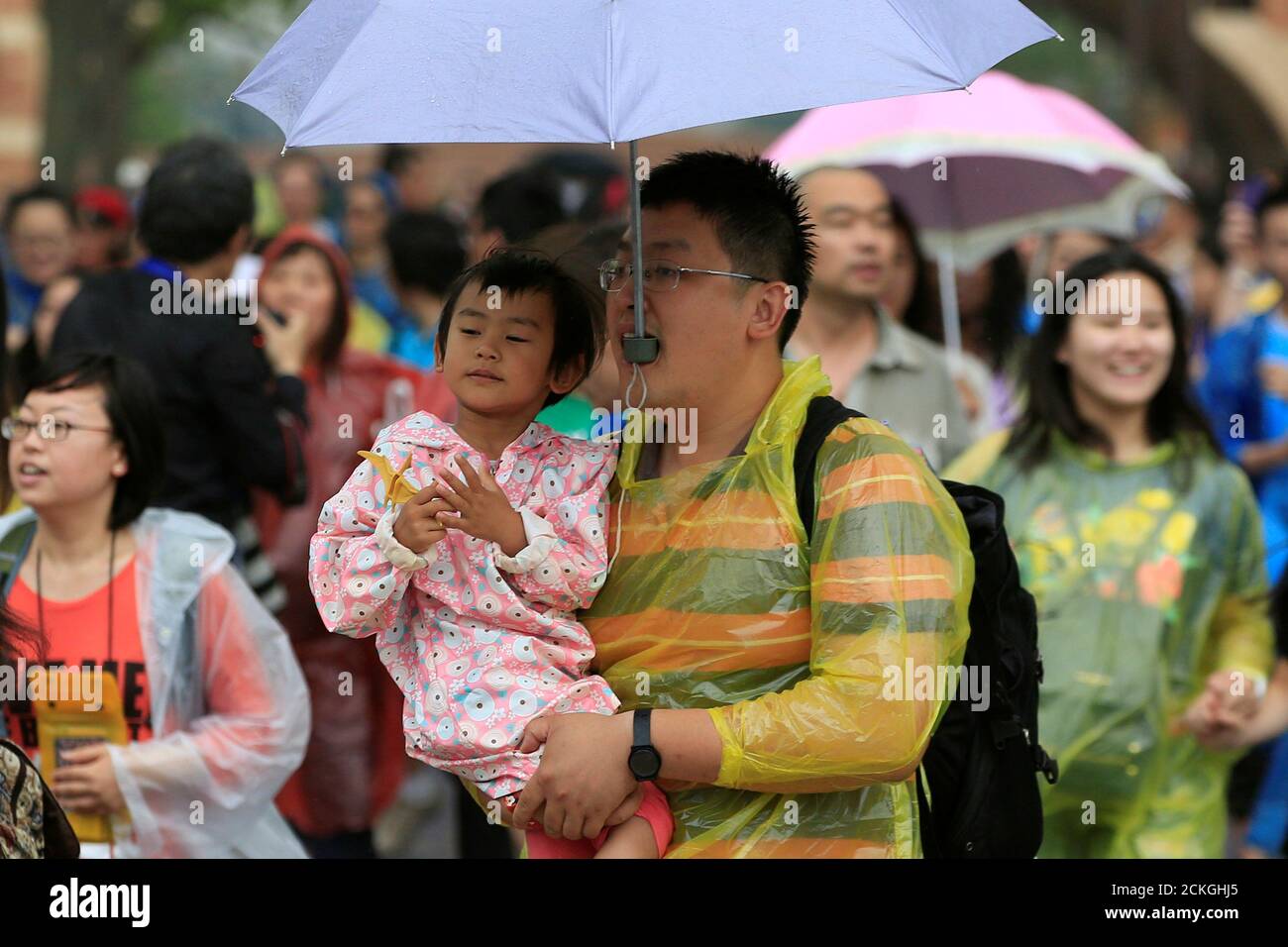 A Man Uses His Mouth To Hold An Umbrella While Carrying A Child As They Enter The Shanghai Disney Resort After The Opening Ceremony Of The Shanghai Disney Resort In Shanghai China