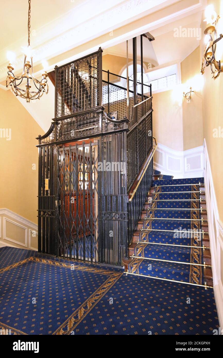 A traditional metal caged lift in the stairwell of a London apartment block. Newly refurbished, shows new carpet, stair rails and ornate lighting. Stock Photo