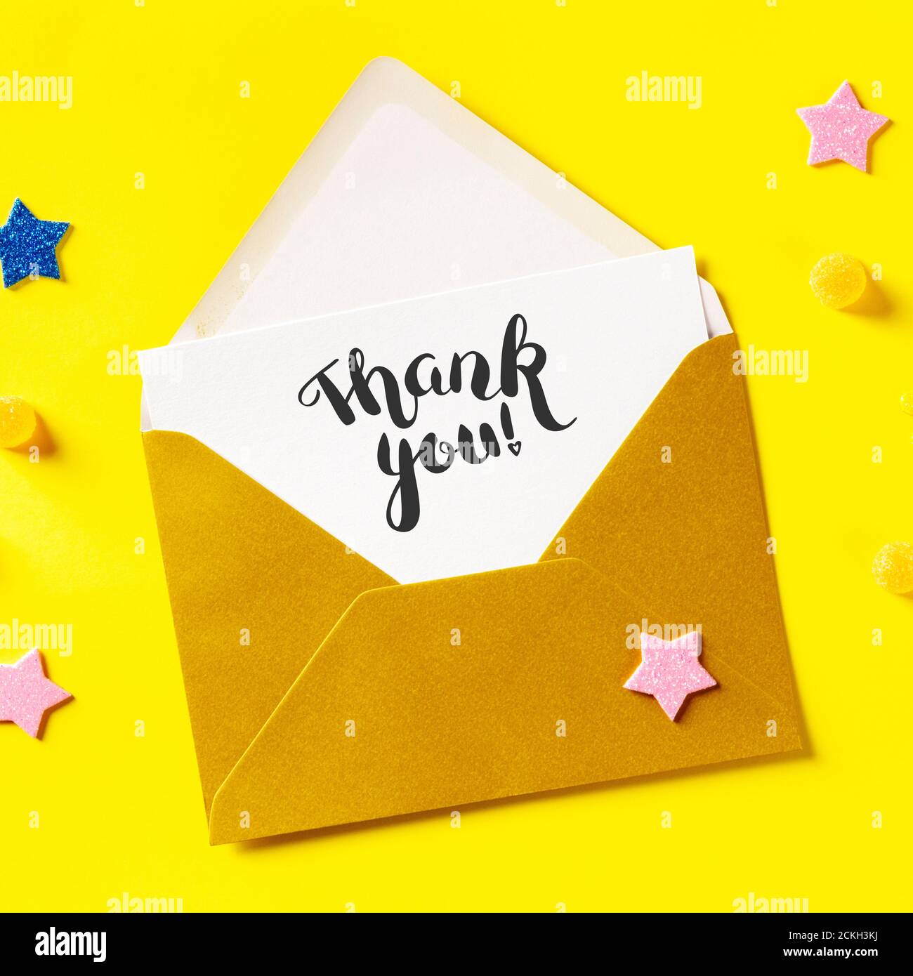 Thank you card in a golden envelope, overhead square shot on a yellow background with glitter stars Stock Photo