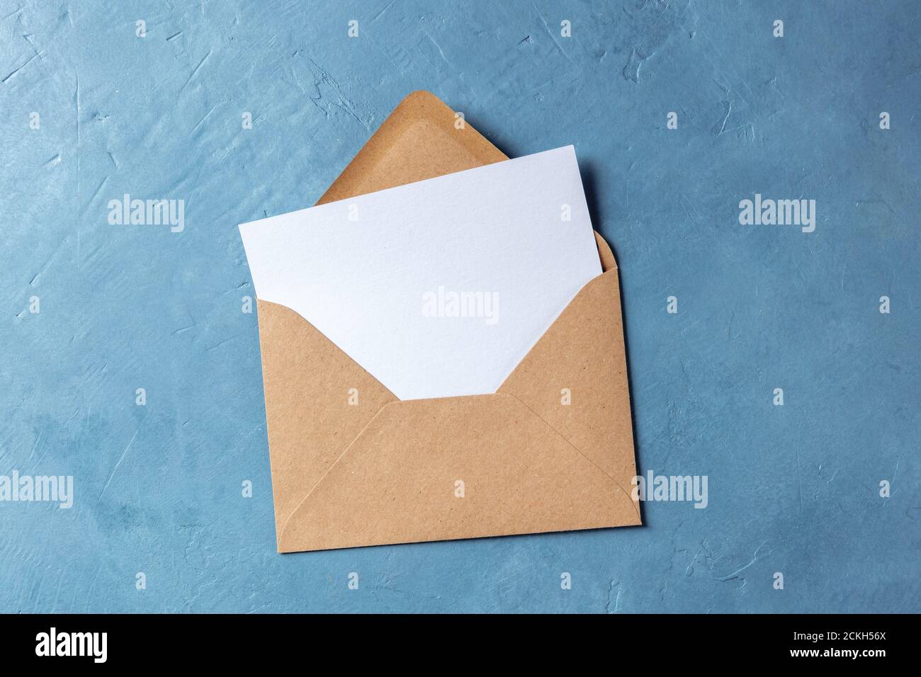 Autumn stationery mockup, overhead flat lay shot of a greeting card or invitation in a brown craft envelope on a blue background Stock Photo
