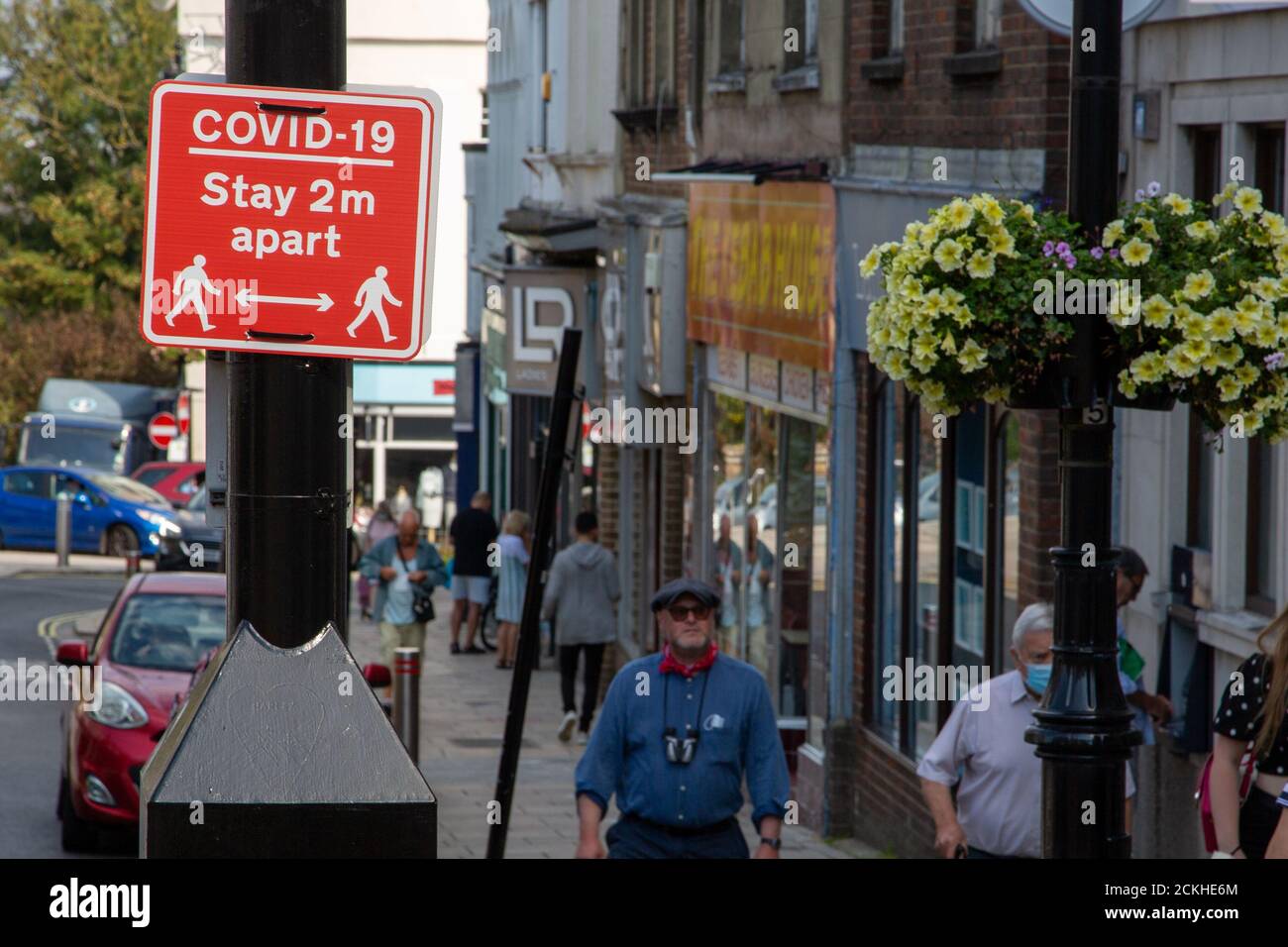 People walking past a sign in the street that states covid-19 stay two meters apart Stock Photo
