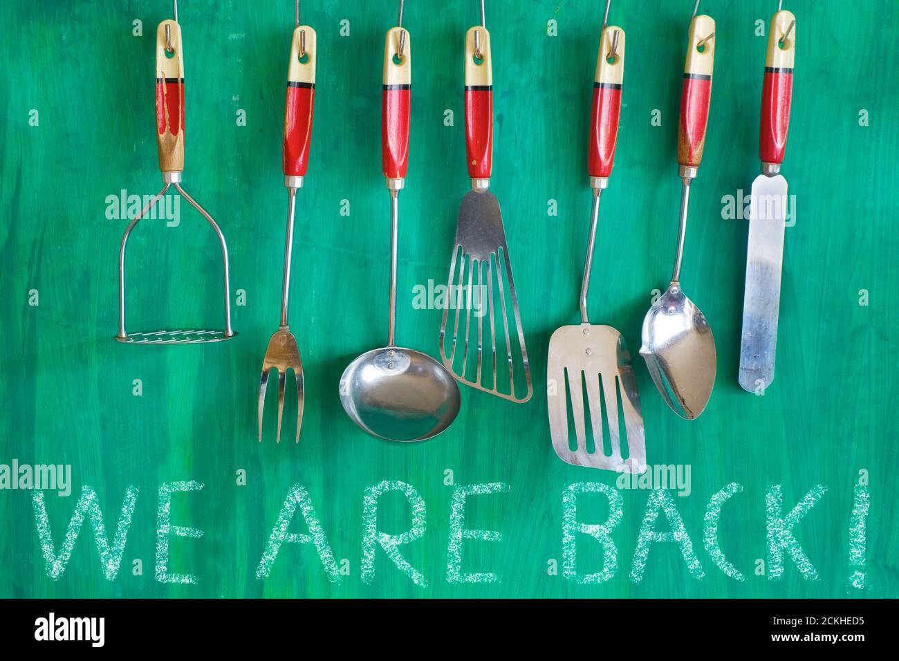 restaurant kitchen utensils on green painted wall, with message we are back. Restart gastronomy business after covid-19 lockdown Stock Photo