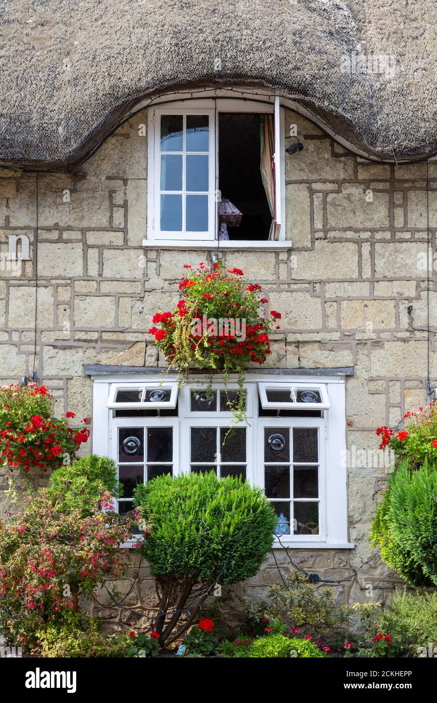 A close up of an exterior of an old thatched cottage with hanging baskets and flowers in front Stock Photo