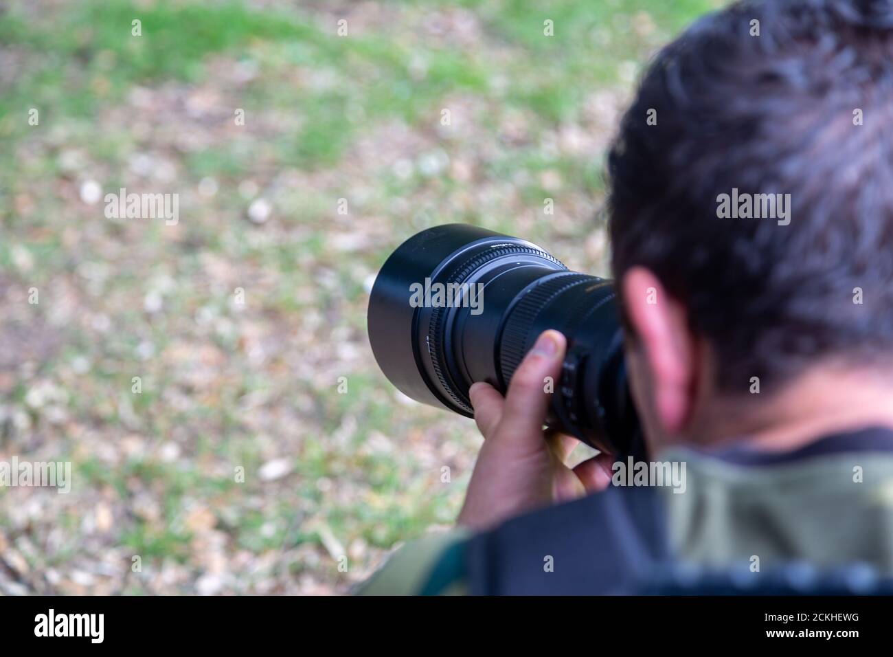 A photographer using a zoom lens with the focus on the lens and the photographer blurred Stock