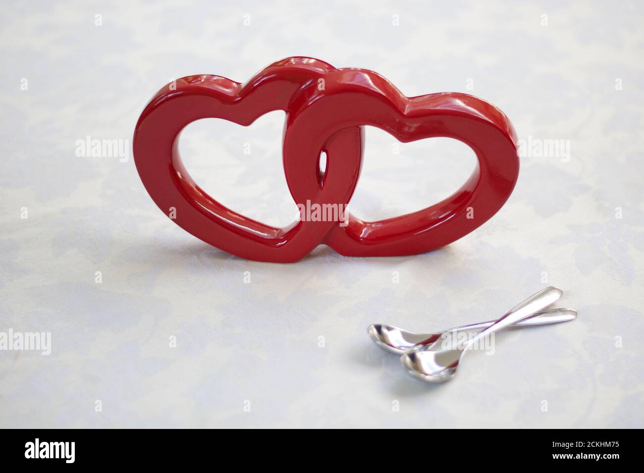 Two intertwined red hearts and a pair of silver teaspoons Stock Photo