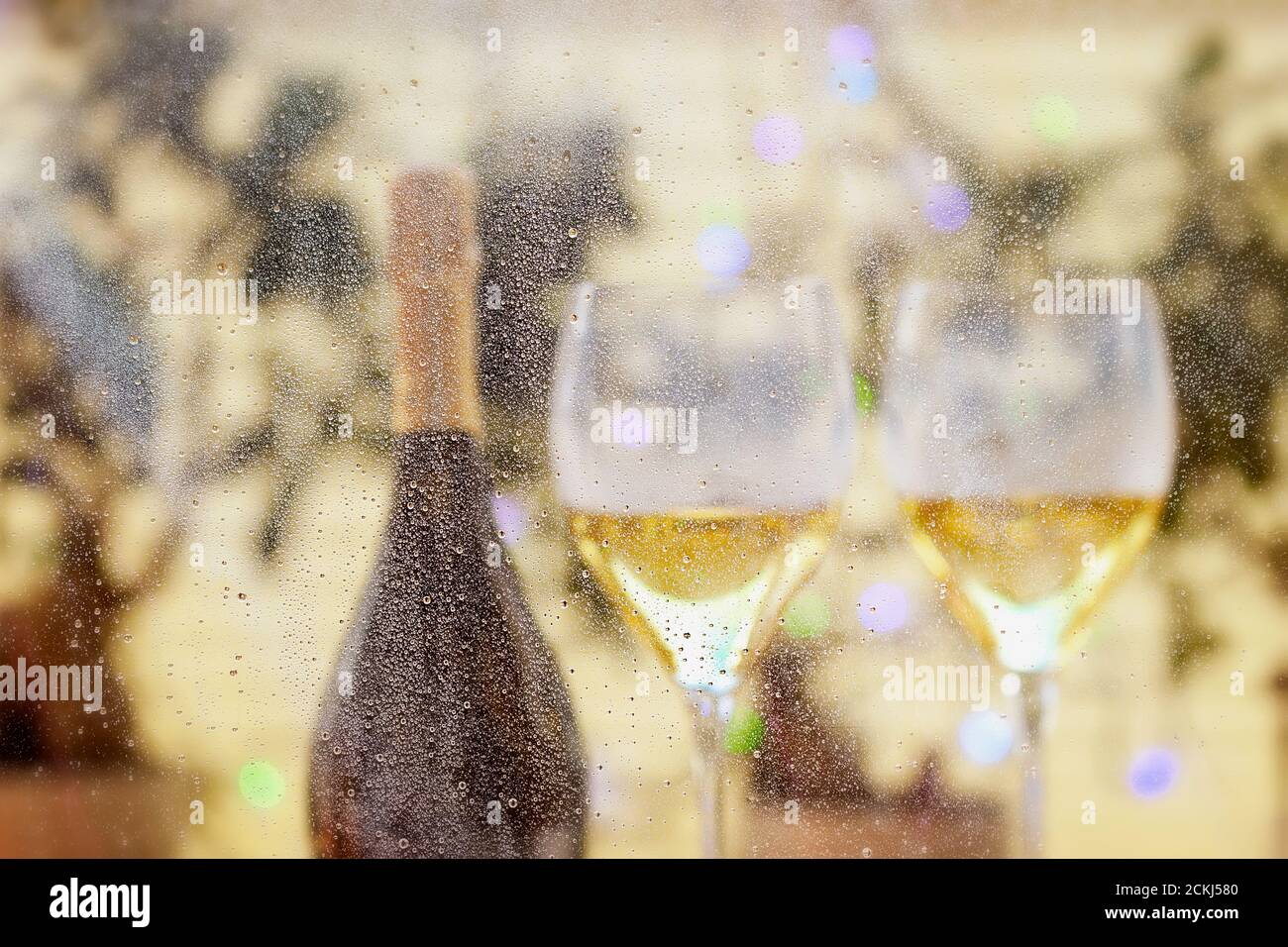 Blurred golden background with two glasses of sparkling wines, bottle, bokeh. Happy New Year Celebration. Selective focus and small depth of field. Stock Photo
