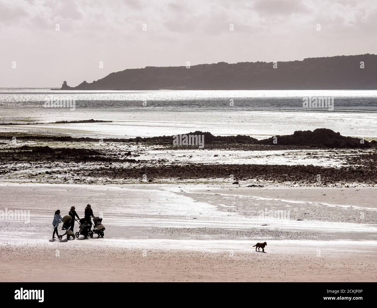 Three women with child buggies walking along a beach in Jersey, Channel
