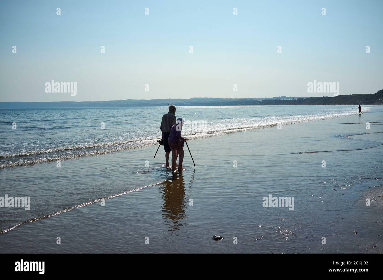 An old couple paddling in the sea on the beach at Filey Cobble Landing, North Yorkshire east coast, northern England, UK Stock Photo