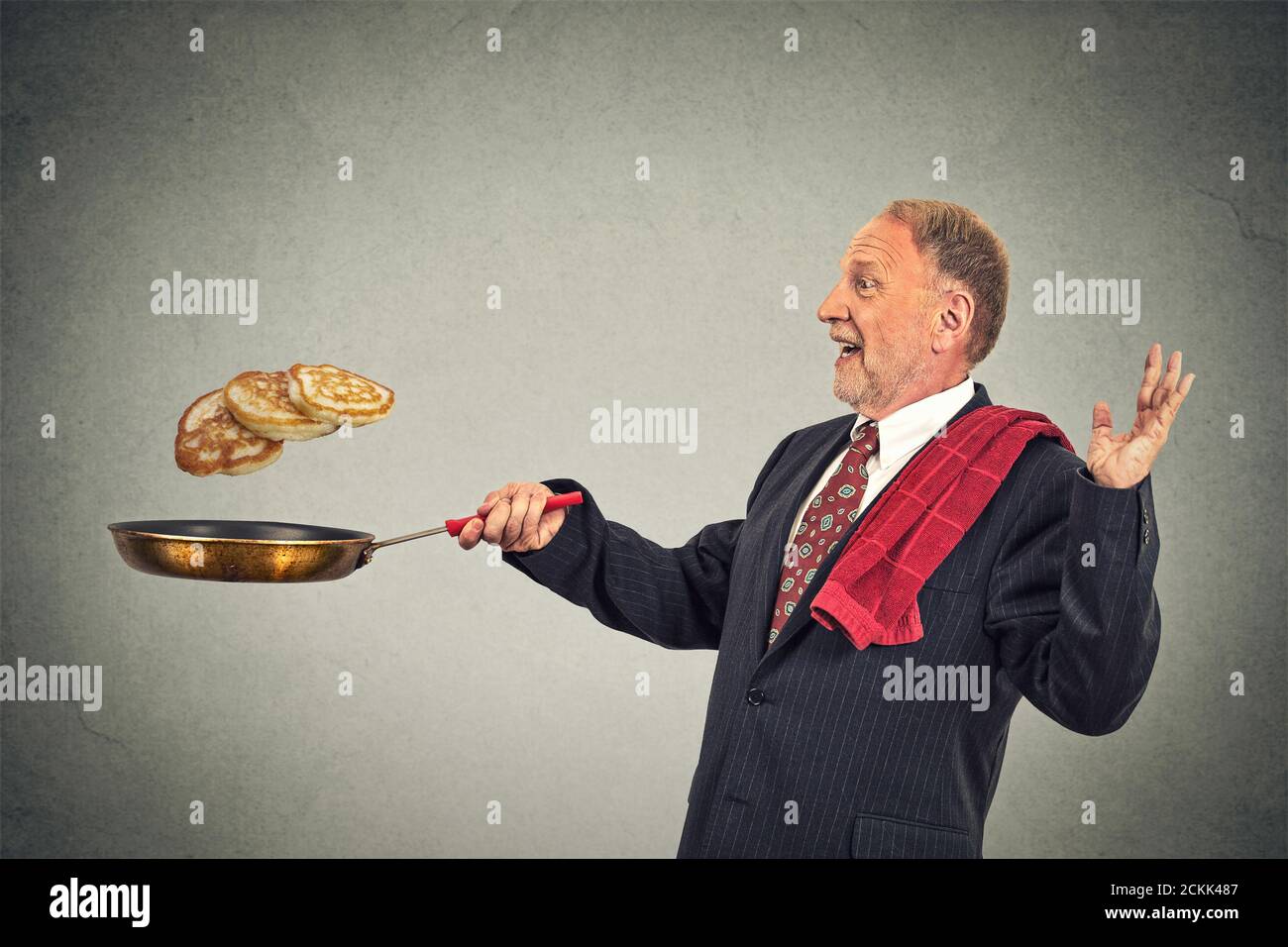 Happy smiling senior man tossing pancakes on frying pan isolated on