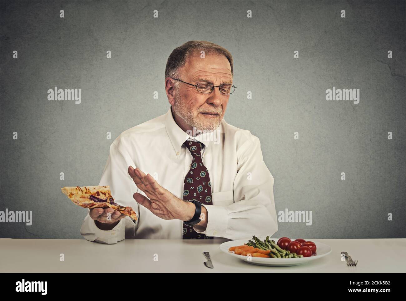 Say no to fast food. Senior man eating fresh vegetable salad avoiding fatty pizza Stock Photo