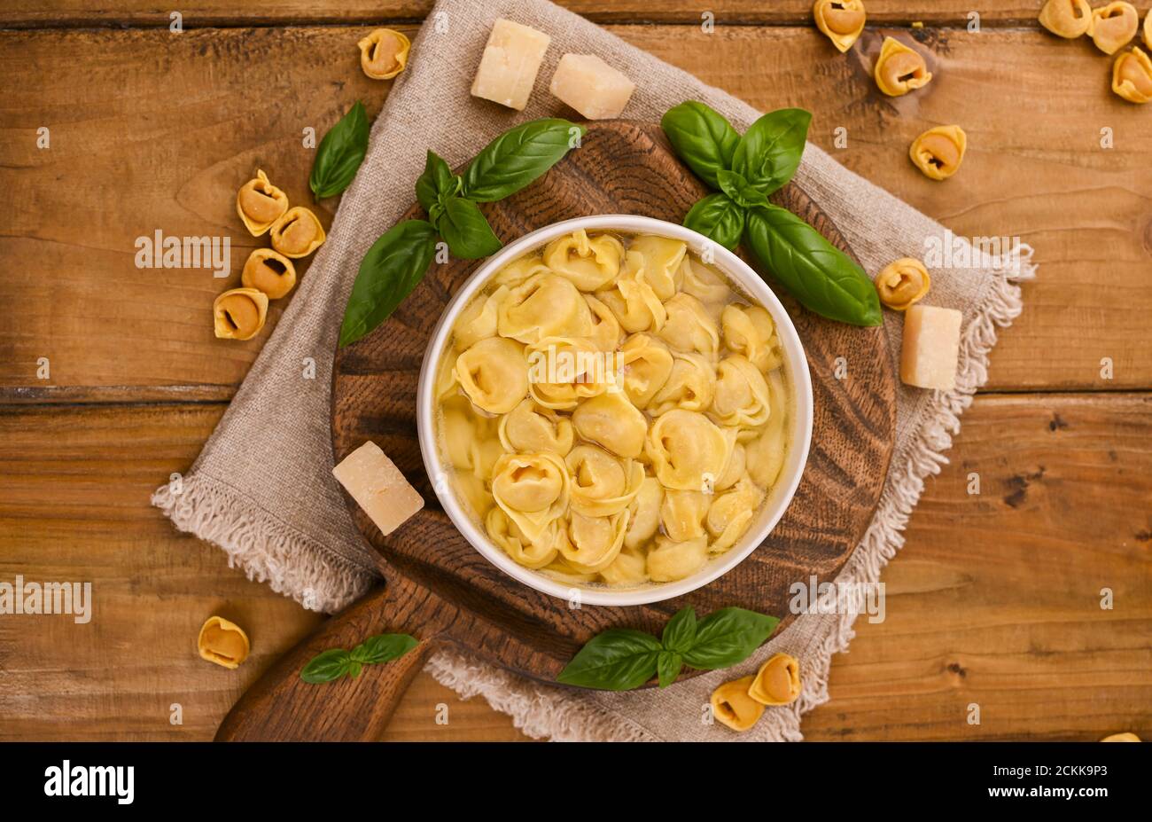 Tortellini mignon on a wooden board with basil and parmesan. Specialties of the cuisine from Bologna and Emilia Romagna: Cappelletti, fresh egg pasta with meat and vegetables filling. Copy space Stock Photo