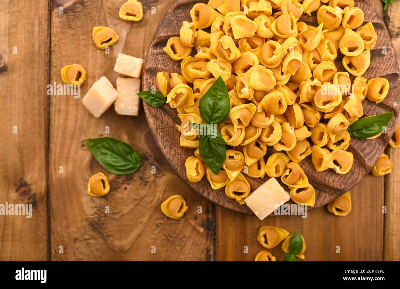 Tortellini mignon on a wooden board with basil and parmesan. Specialties of the cuisine from Bologna and Emilia Romagna: Cappelletti, fresh egg pasta with meat and vegetables filling. Copy space Stock Photo