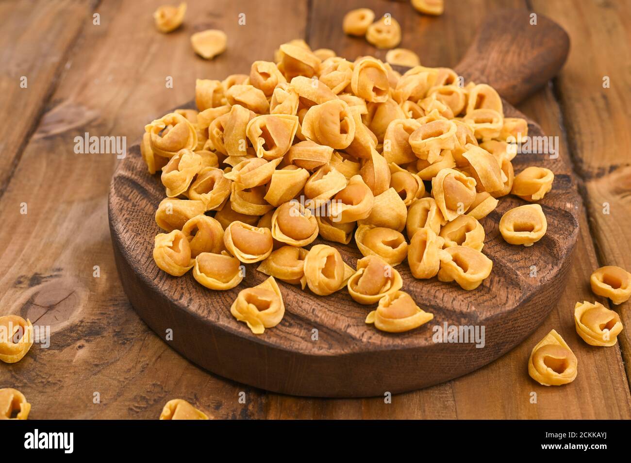 Tortellini mignon on a wooden board and parmesan. Specialties of the cuisine from Bologna and Emilia Romagna: Cappelletti, fresh egg pasta with meat and vegetables filling. Copy space Stock Photo