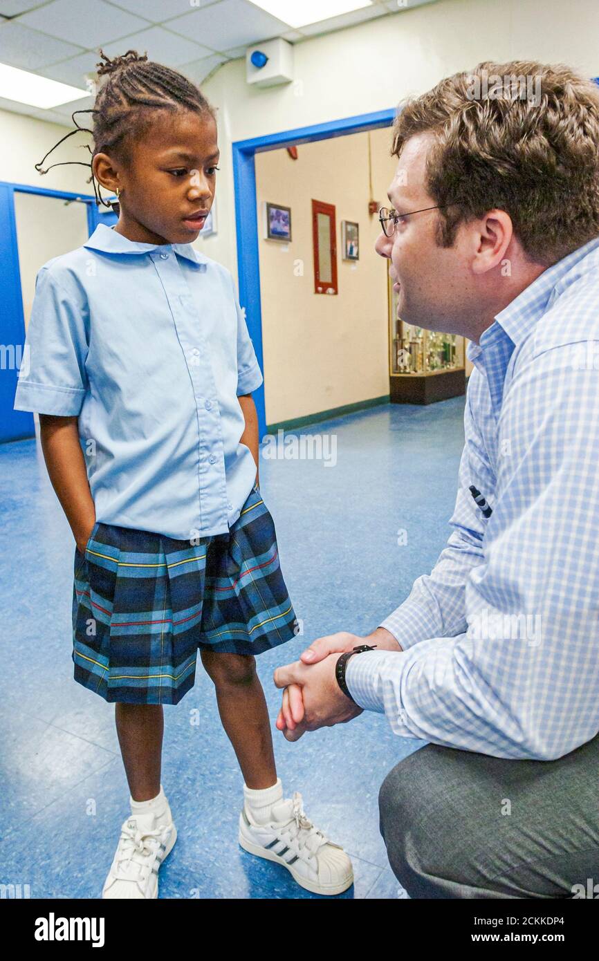 Miami Florida,Frederick Douglass Elementary School,low income Black student girl talking with,class classroom visitor man from law firm donating books Stock Photo