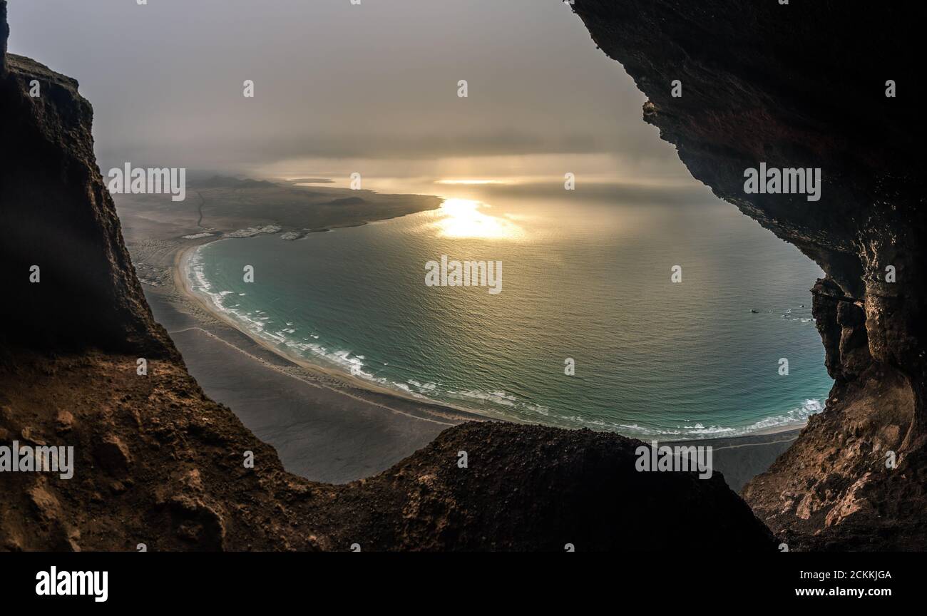 viewpoint over Famara beach at sunset with cloudy sky and sun rays coming out of the clouds, Cueva de las Cabras, Lanzarote island, Canary Islands, Sp Stock Photo