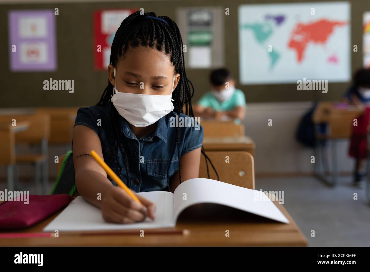Girl wearing face mask writing while sitting on her desk at school Stock Photo