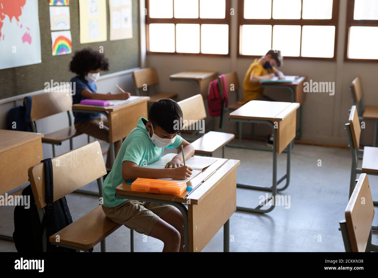 Group of kids wearing face masks writing while sitting on their desk at school Stock Photo
