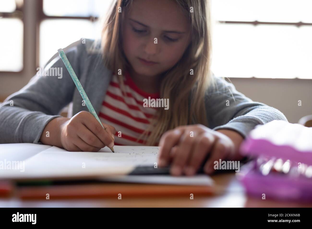 Girl writing in a book while sitting on her desk at school Stock Photo