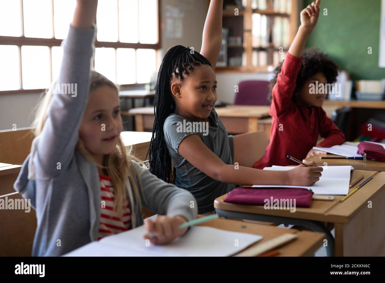 Group of kids raising their hands while sitting on their desk at school Stock Photo