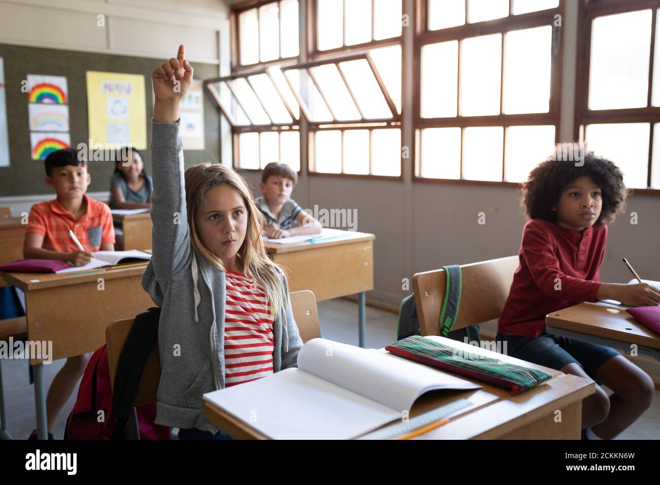 Girl raising her hand while sitting on her desk at school Stock Photo