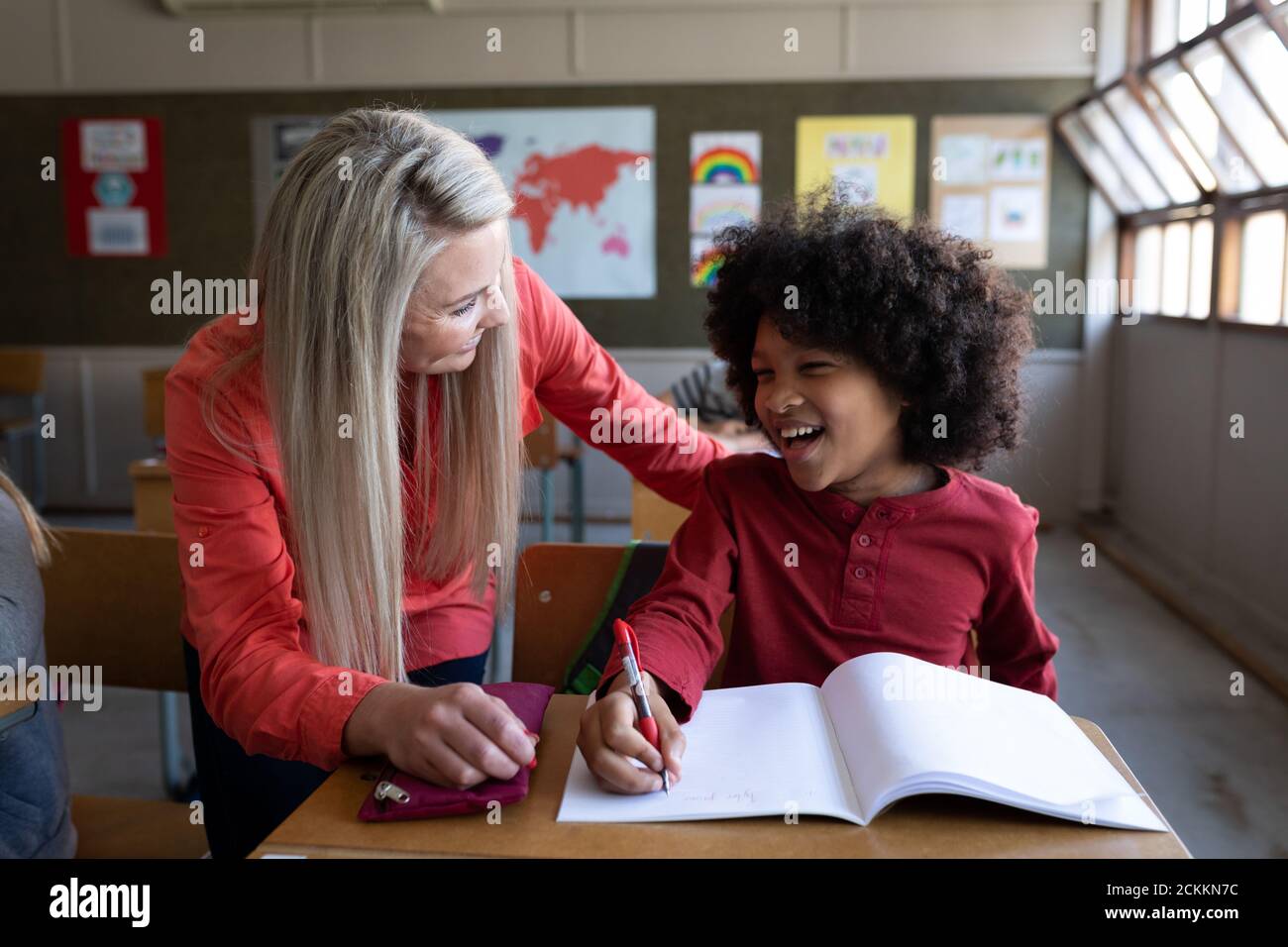 Female teacher helping a boy to write in a book in class at school Stock Photo