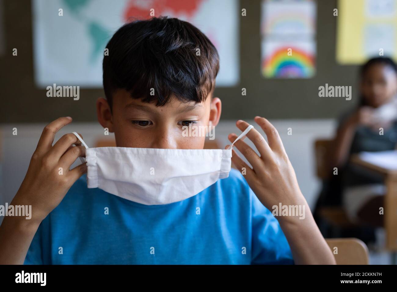 Boy wearing face mask while sitting on his desk at school Stock Photo