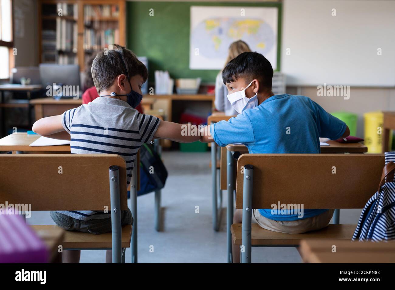 Two boys wearing face masks greeting each other by touching elbows at school Stock Photo