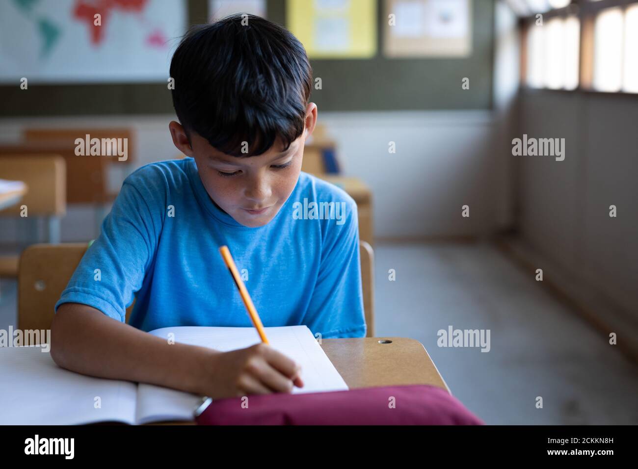 Boy writing in a book while sitting on his desk at school Stock Photo
