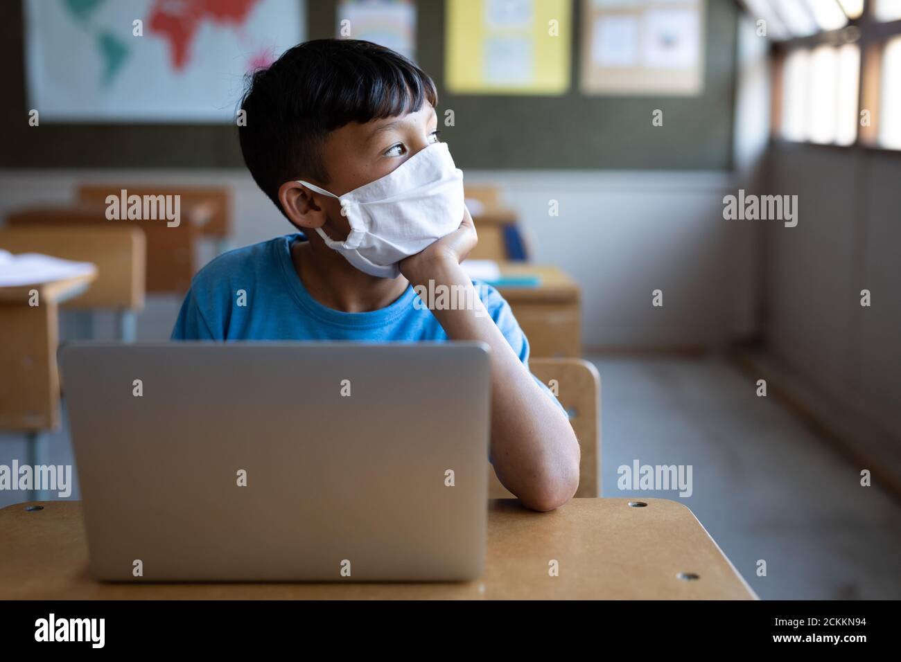 Boy wearing face mask sitting with laptop on his desk at school Stock Photo