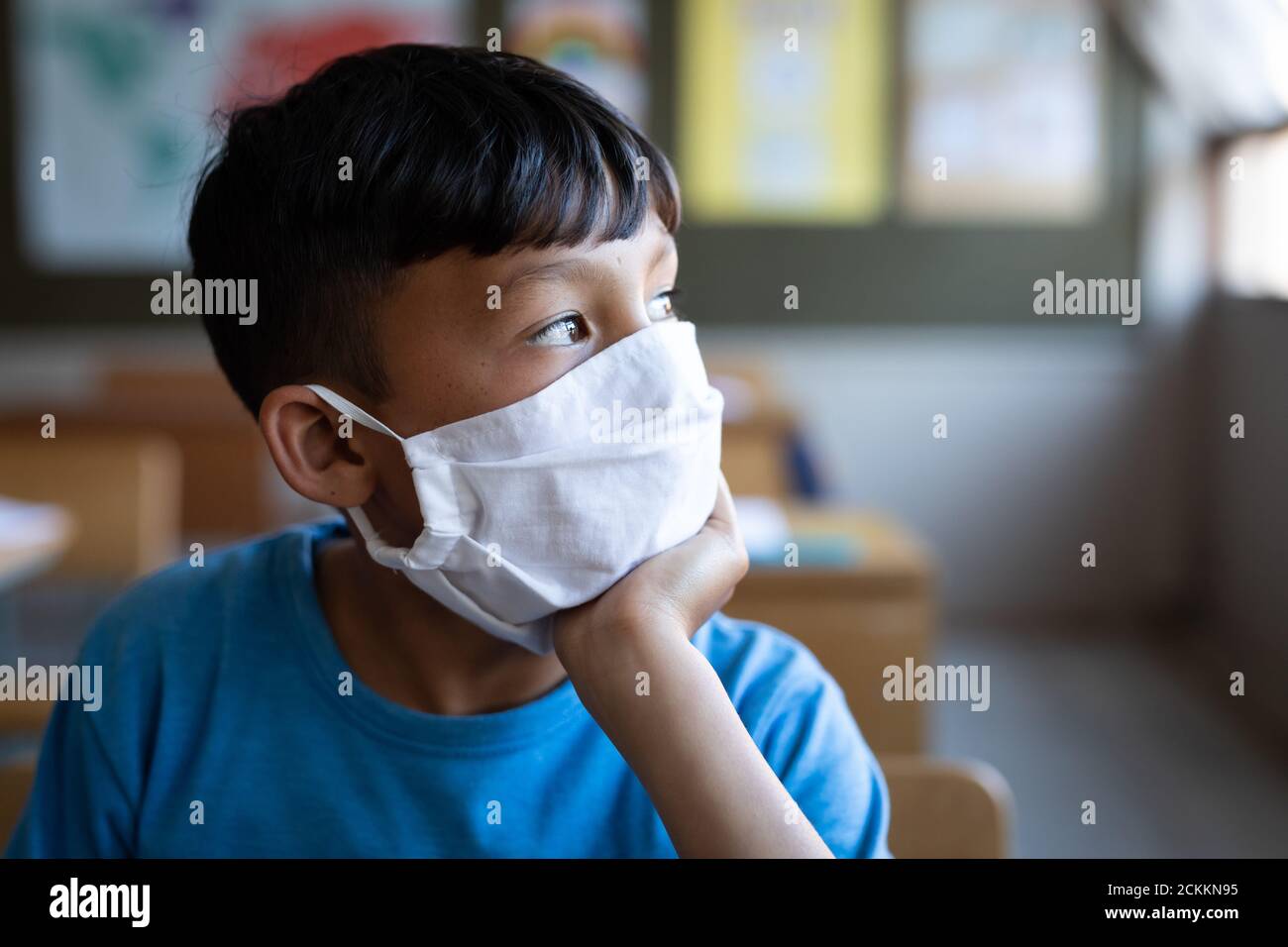 Boy wearing face mask sitting on his desk at school Stock Photo