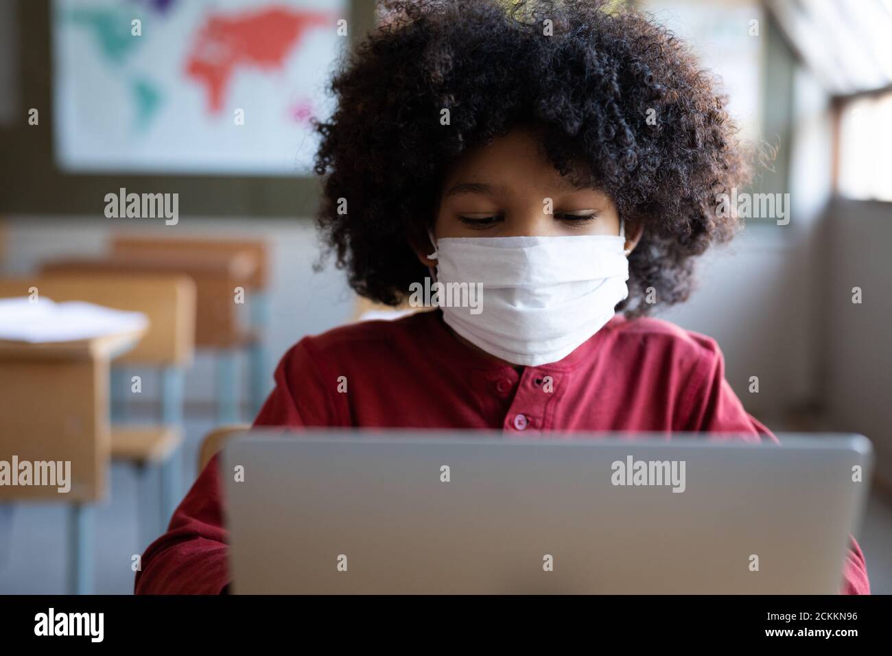 Boy wearing face mask using laptop on his desk at school Stock Photo