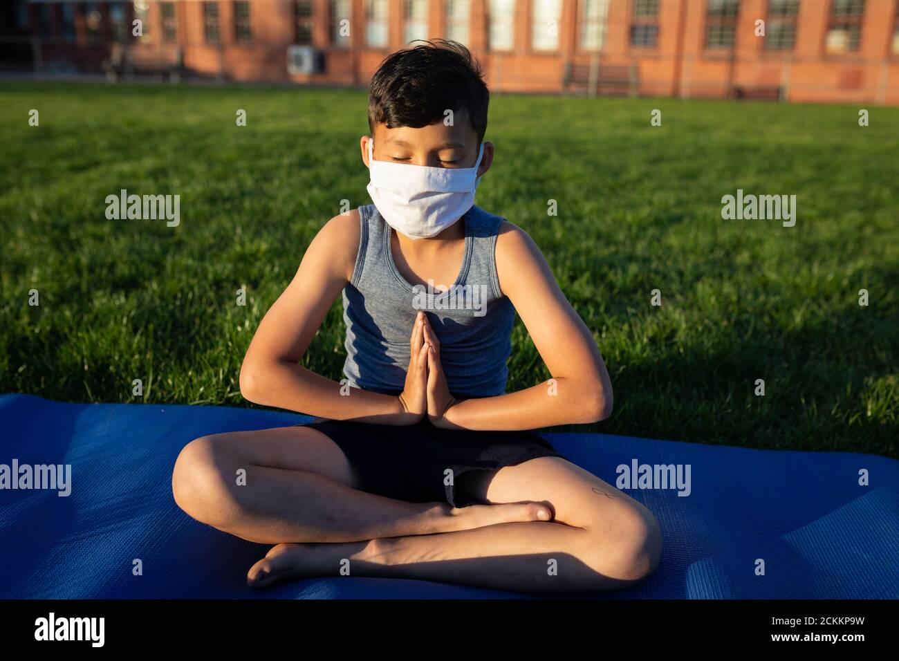 Boy wearing face mask performing yoga in the garden Stock Photo